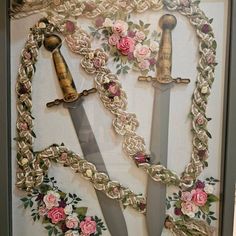 two large swords with flowers on them are in a shadow box, surrounded by chains and roses