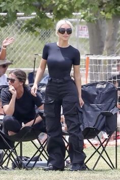 a woman in black pants and sunglasses standing next to a soccer ball on a field