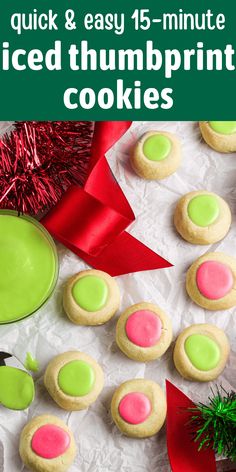 green and pink iced thumbprint cookies on white paper next to red ribbon, christmas decorations