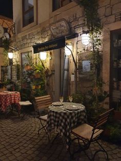 an outdoor dining area at night with tables and chairs covered in checkered tablecloths