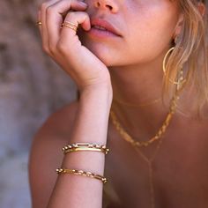 a close up of a person wearing gold jewelry and holding her hand near her face