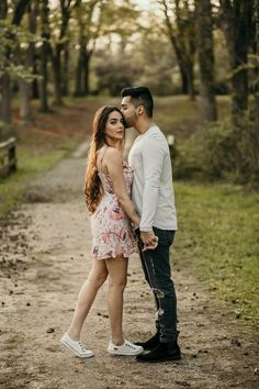 a man and woman standing next to each other on a dirt road in the woods