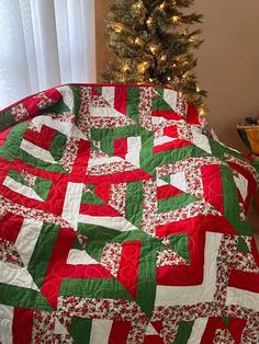 a quilted christmas tree sits in front of a window with a red and green blanket on it