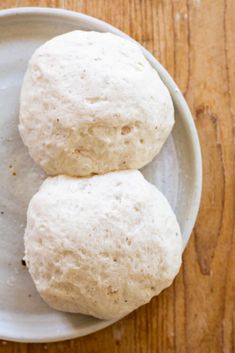 two uncooked buns on a white plate next to a wooden table top