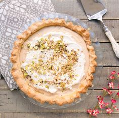 a pie sitting on top of a wooden table next to a knife and fork with flowers in the background