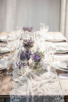 the table is set with purple flowers in vases