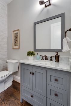 a white toilet sitting next to a bathroom sink under a mirror on top of a wooden floor