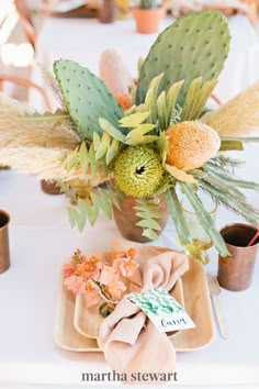 an arrangement of flowers and succulents on a white table cloth with napkins