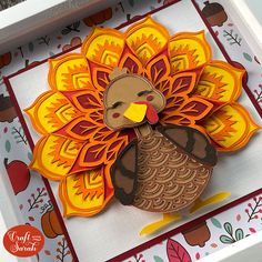 a paper turkey is sitting in a white box with red and yellow trimmings