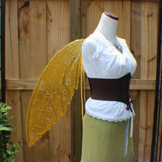 a dress made to look like a butterfly with wings on it's back, sitting in front of a wooden fence