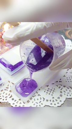 a person pouring purple liquid into a glass on top of a doily covered table