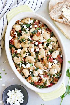 a casserole dish with spinach, feta cheese and bread on the side