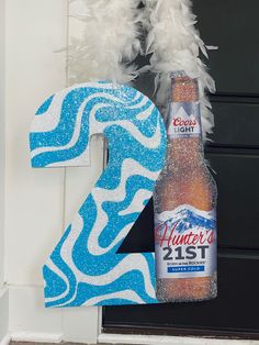 the number two is decorated with feathers and a bottle of beer in front of it