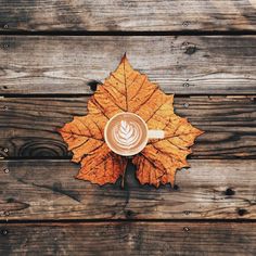 a cup of coffee sitting on top of a wooden table next to an orange leaf