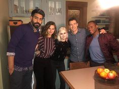 a group of people posing for a photo in a kitchen with fruit on the counter