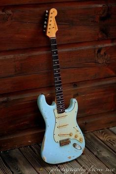 an electric guitar sitting on top of a wooden floor next to a wall with wood planks