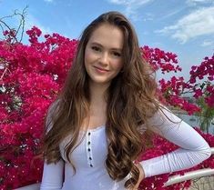 a woman standing in front of pink flowers with her hands on her hips and looking at the camera