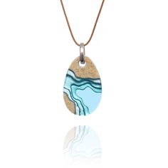 Each purchase from our Aqua Collection will help provide one year of safe water to one person in need through BoldB's support of Water.org, an international nonprofit organisation. Cove - a small and sheltered bay or inlet -Our small cove pendant has been carefully handmade from bonded beach sand, aqua blue resin and metal pigments with a high-gloss polished finish. -A free-swinging hook connects the pendant to its cord -76 cm long caramel brown cotton cord with sliding knot to adjust the length Ocean-inspired Round Pendant Jewelry, Ocean-inspired Blue Round Pendant Jewelry, Turquoise Resin Pendant Necklace, Blue Resin Ocean-inspired Necklace, Blue Resin Necklaces With Ocean-inspired Style, Caramel Brown, Beach Necklaces, Sliding Knot, Beach Sand