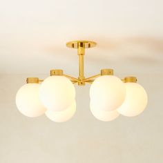 three white balls are hanging from a brass ceiling light in a room with beige walls