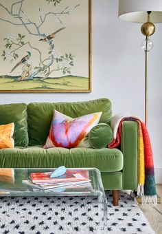 a living room with a green couch and colorful pillows on the sofa, next to a painting