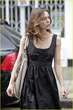 a woman in a black dress is walking down the street