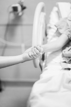 a person in a hospital bed holding the hand of another person who is laying down