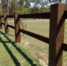 a wooden fence is shown with grass and trees in the background, along with a tennis court