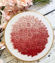 a close up of a embroidery on a wooden surface with pink flowers in the background