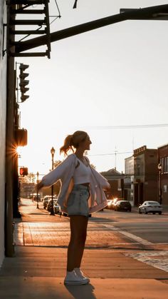 a woman standing on the side of a road next to a traffic light with her arms outstretched