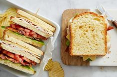 two trays filled with sandwiches and chips on top of a white marble countertop