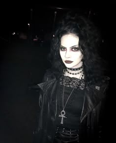 a woman with black hair and makeup is dressed in goth clothing, wearing gothic jewelry