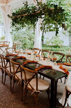 a long table set up with place settings and napkins for dinner under an arbor