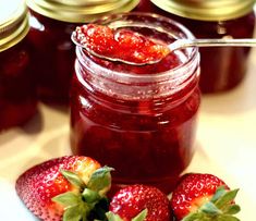 two strawberries sit next to jars of jam