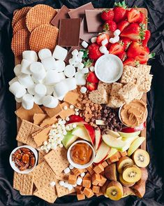 a platter filled with fruit, marshmallows, and crackers on top of a black cloth