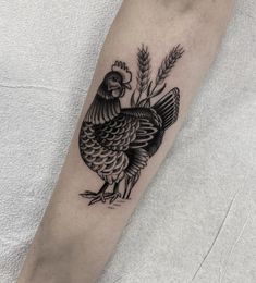 a black and white tattoo of a chicken on the left arm with wheat sprouts