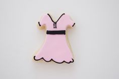 a cookie shaped like a pink dress with black trim on the front and back, sitting on a white surface