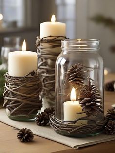 three mason jars filled with pine cones and candles sitting on top of a wooden table