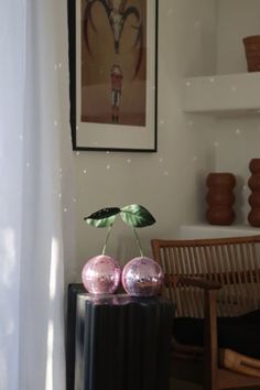 two pink balls sitting on top of a black table next to a chair and painting