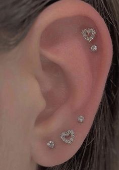 a woman's ear with three heart shaped studs on the middle of it