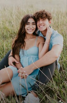 a man and woman are sitting in the grass smiling at the camera, with their arms around each other