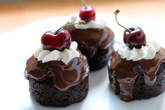 three chocolate cupcakes topped with whipped cream and cherries on a white plate