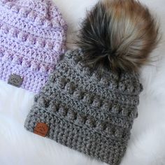 two crocheted hats with pom - poms laying on top of each other