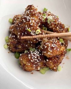 a white plate topped with meatballs covered in sesame seeds and green onions next to a wooden spoon