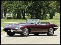 an old fashioned sports car parked on the side of the road with trees in the background