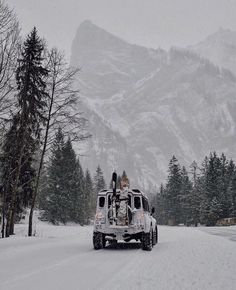 a truck driving down a snow covered road in front of a large mountain range with trees