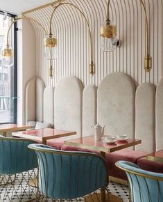 the interior of a restaurant with pink and blue chairs, gold accents and white walls