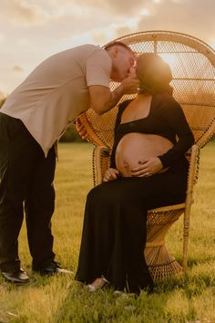 a man kissing a pregnant woman on the cheek while sitting in a wicker chair