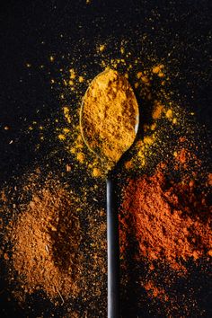 a spoon full of powdered spices next to an orange and brown substance on a black surface