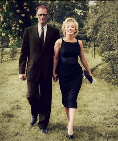 a man and woman are walking in the grass holding hands, both dressed in black