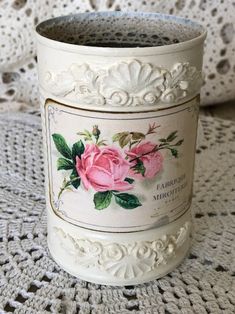 a white crochet doily with a pink rose on it and two jars